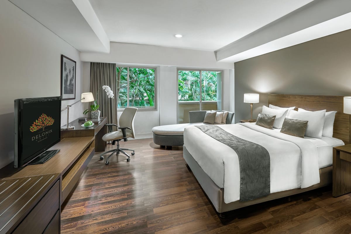 Quarto de hotel com uma cama grande, uma escrivaninha, uma cadeira e uma televisão.