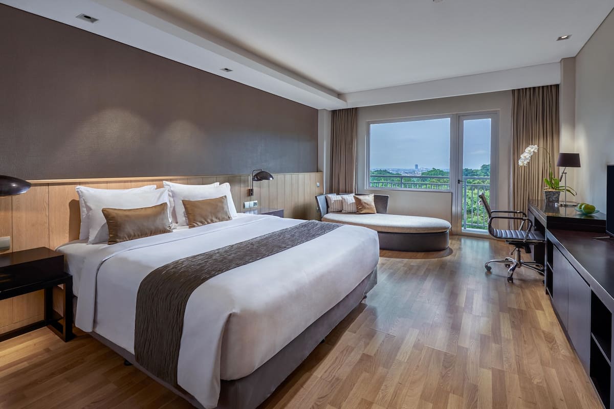 Quarto de hotel moderno com uma cama grande, uma escrivaninha, uma cadeira e uma televisão.