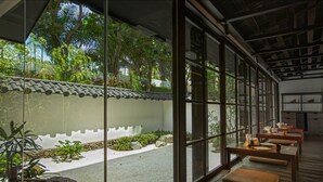 A traditional Japanese-style room with tatami flooring, a low table with cushions, and a view of a garden through large windows. - Delonix Hotel Karawang (Karawang)