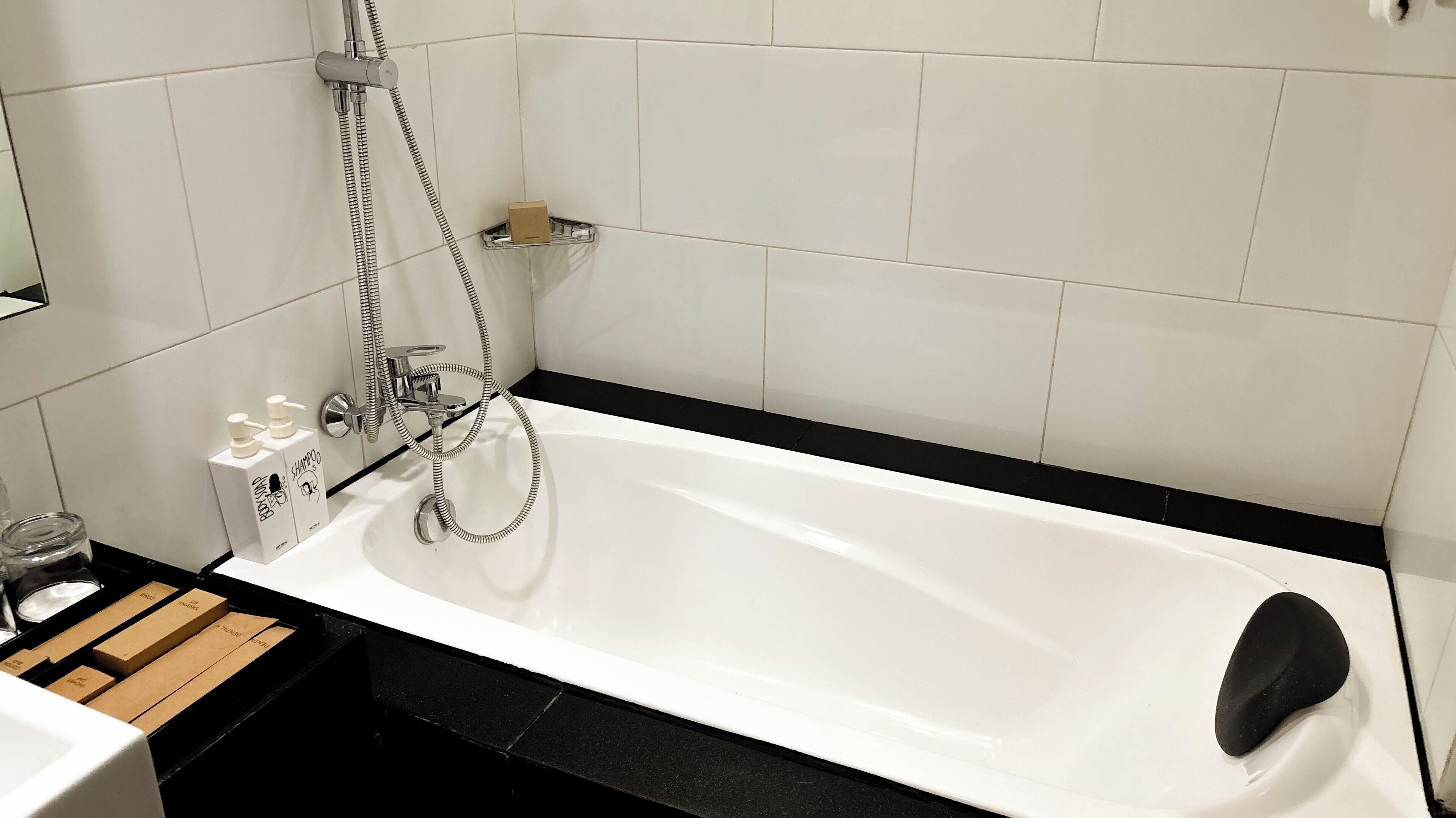 A modern bathroom with a white bathtub, a handheld showerhead, and a soap dispenser.