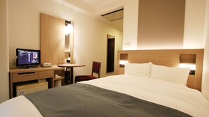 A hotel room with a bed, a desk with a computer, a chair, and a small table.