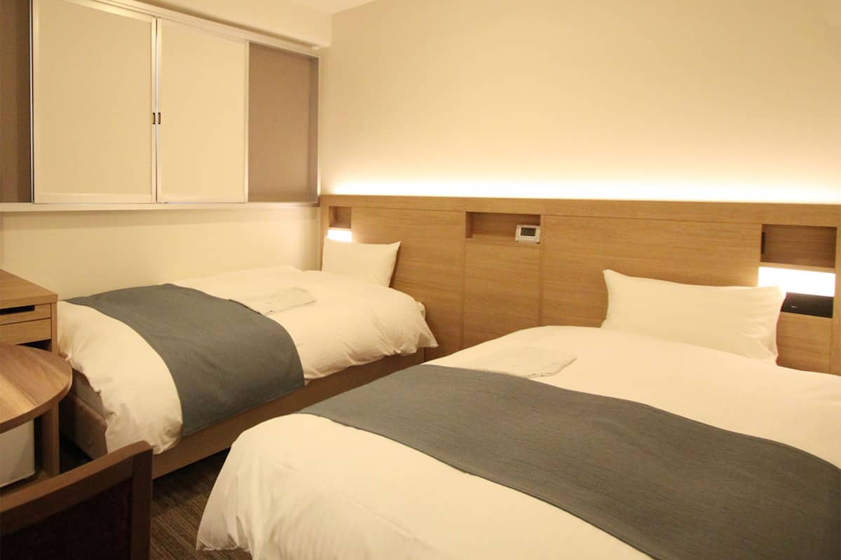 A hotel room with two beds, a wooden headboard, a bedside table, and a wardrobe.