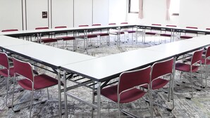 A conference room with a long table and red chairs, white walls, and a carpeted floor.