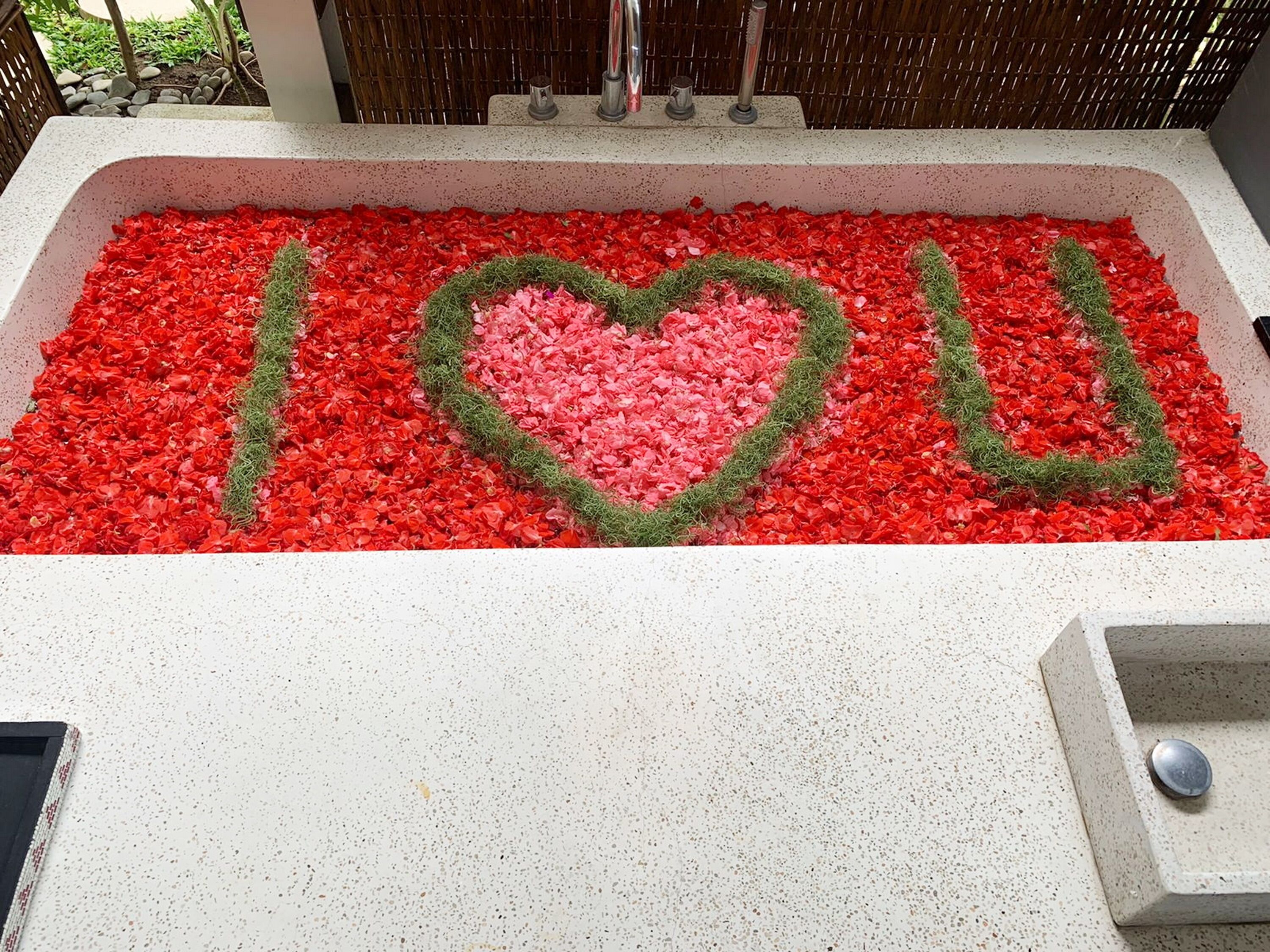 A bathtub with red rose petals arranged to spell "I love you."