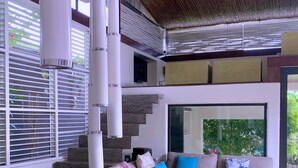 A modern living room with a beige sofa, colorful cushions, and a glass door leading to a balcony. - Kiss Villas Bali (Seminyak)