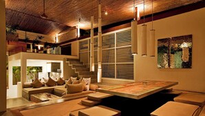 A modern living room with a large coffee table, cushioned seating, and pendant lighting. - Kiss Villas Bali (Seminyak)