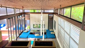 A room with a bamboo ceiling, large windows, blue cushioned seating, and a small table. - Kiss Villas Bali (Seminyak)