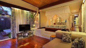 A modern bedroom with a TV, comfortable seating, and a canopy bed. - Kiss Villas Bali (Seminyak)