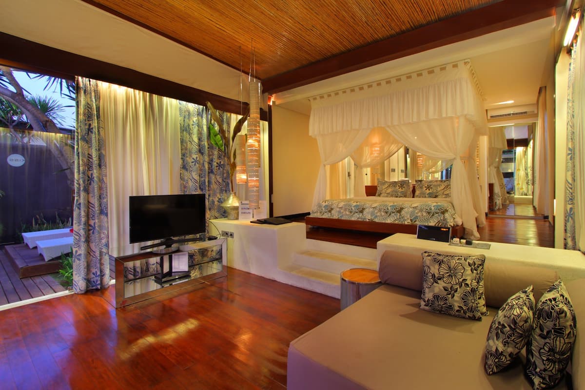 A modern bedroom with a TV, comfortable seating, and a canopy bed.