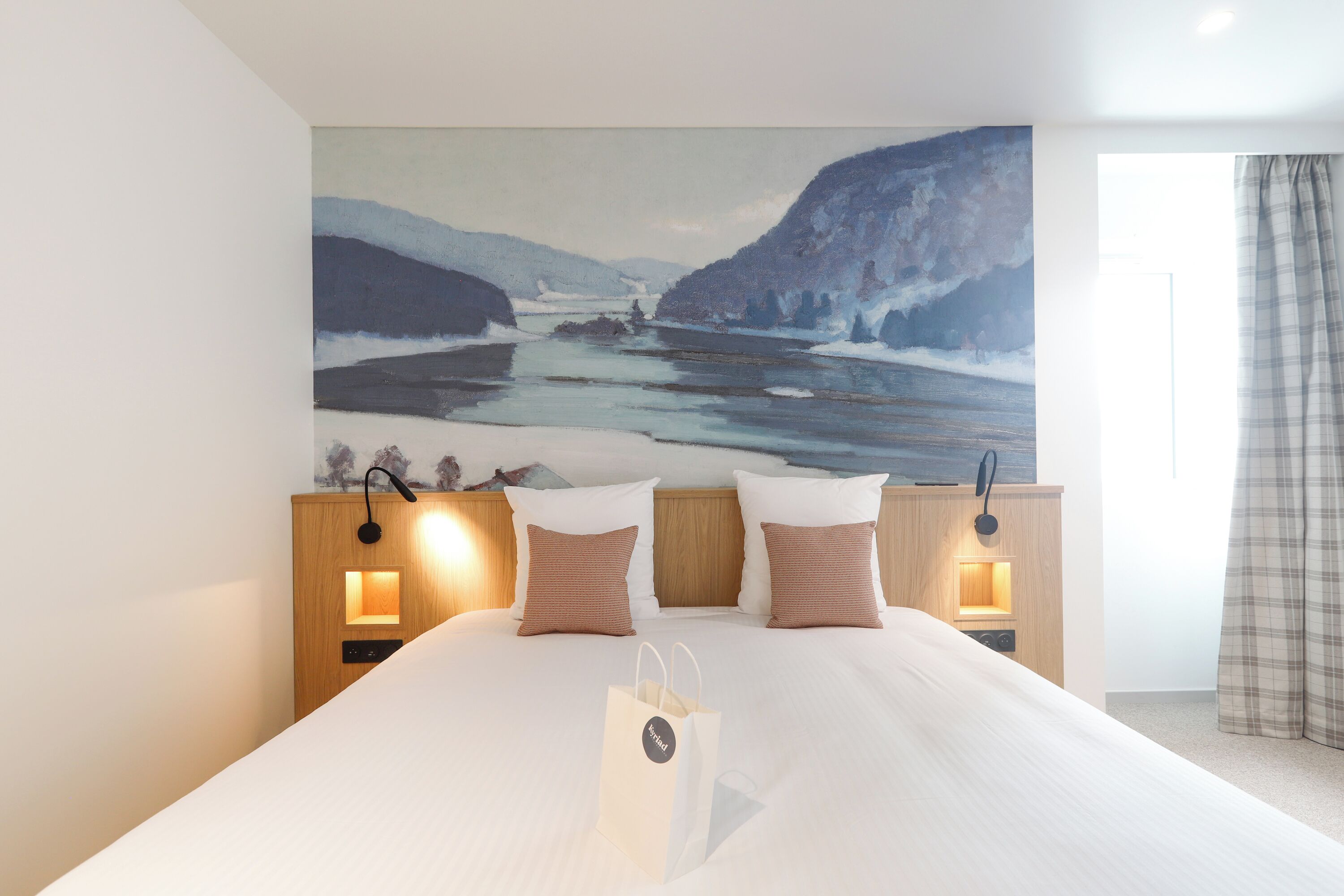 Habitación de hotel con una cama grande, dos lámparas de noche, una mesita de noche y un cuadro de un paisaje.