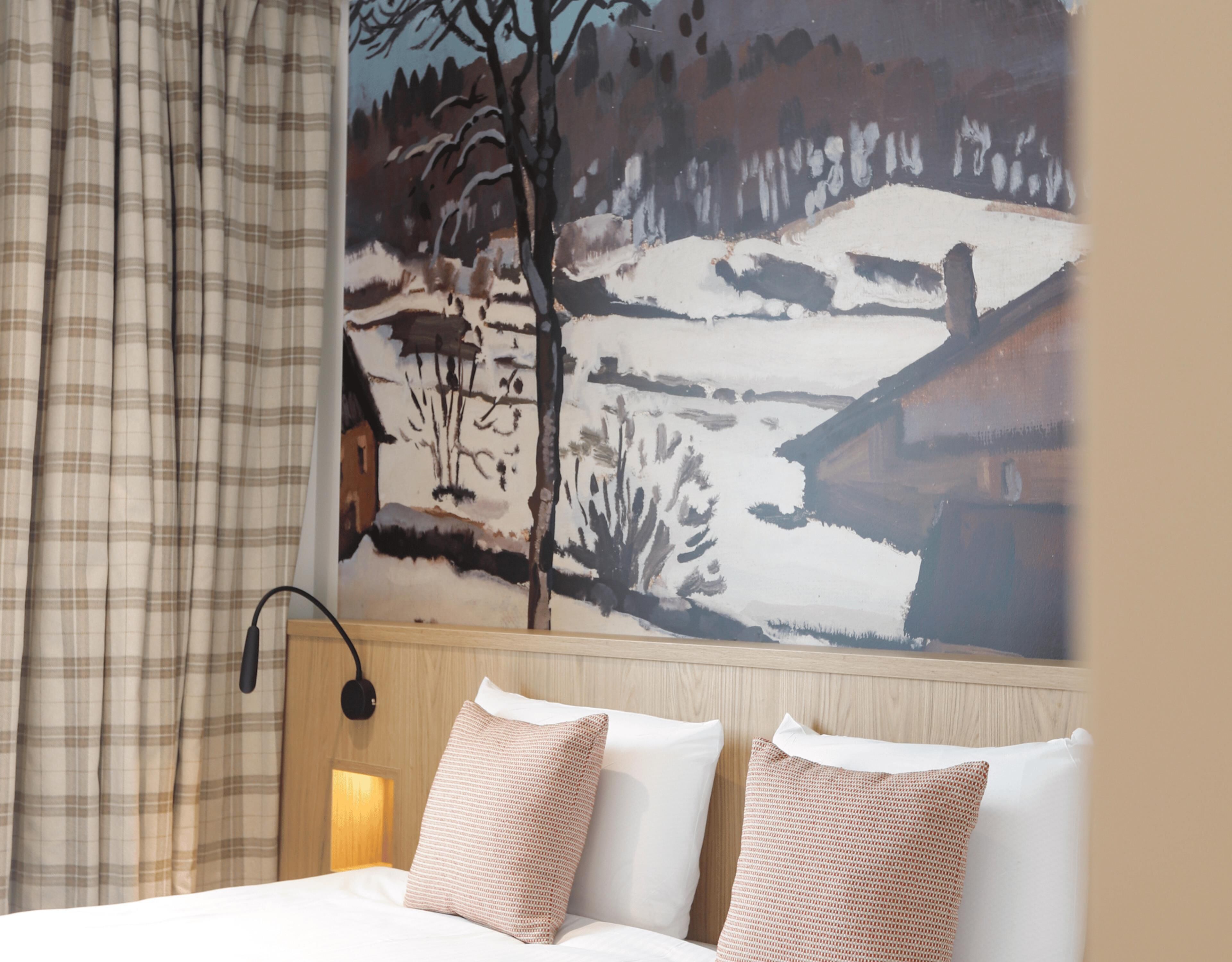 Habitación de hotel con una cama, cortinas a cuadros, una lámpara de pared y un cuadro de un paisaje nevado.