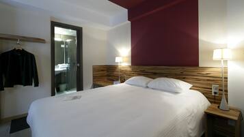 Une chambre d’hôtel avec un lit, des lampes de chevet, une tête de lit en bois, un porte-manteau et un miroir.