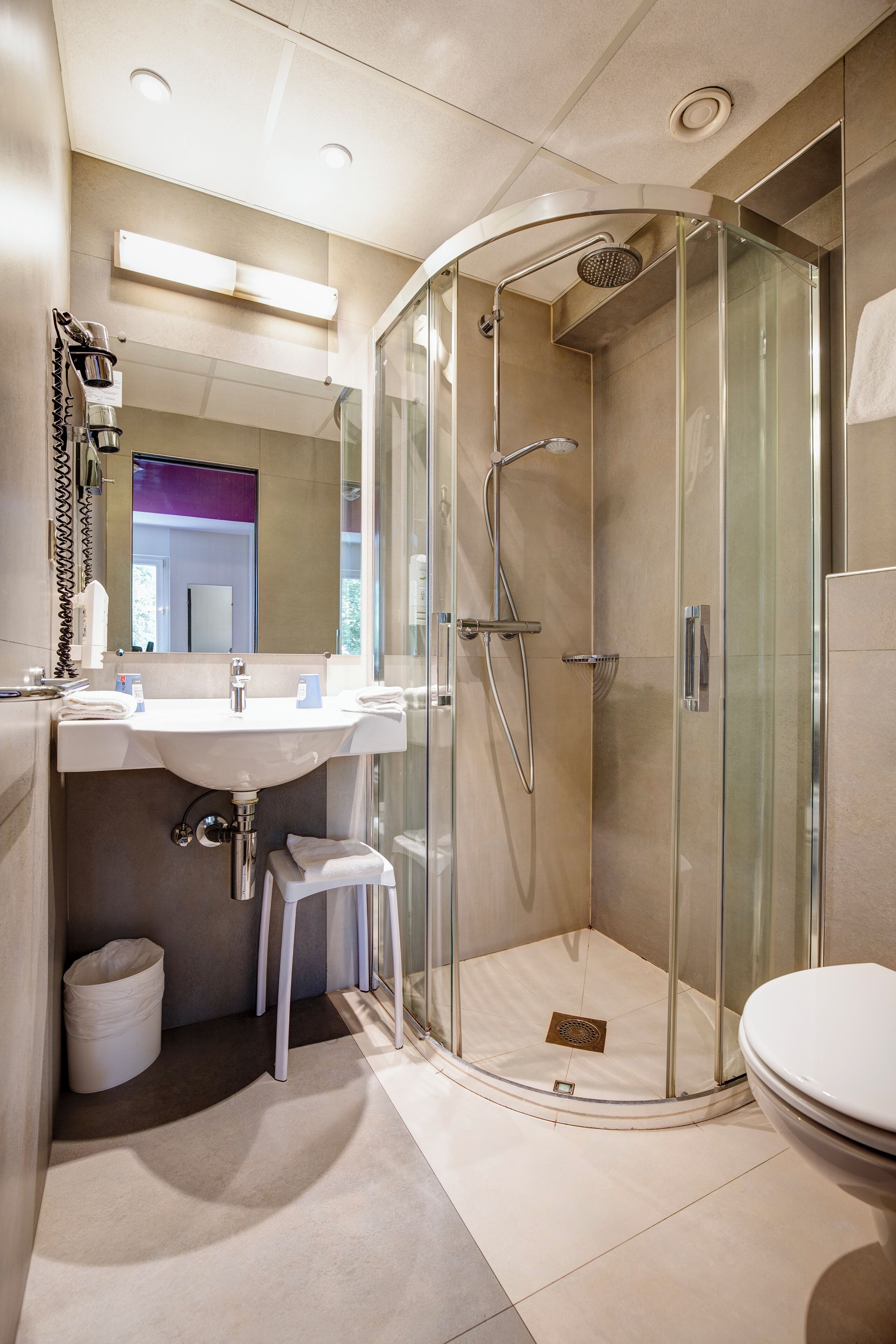 Un baño moderno con ducha de vidrio, un lavamanos blanco y un inodoro.