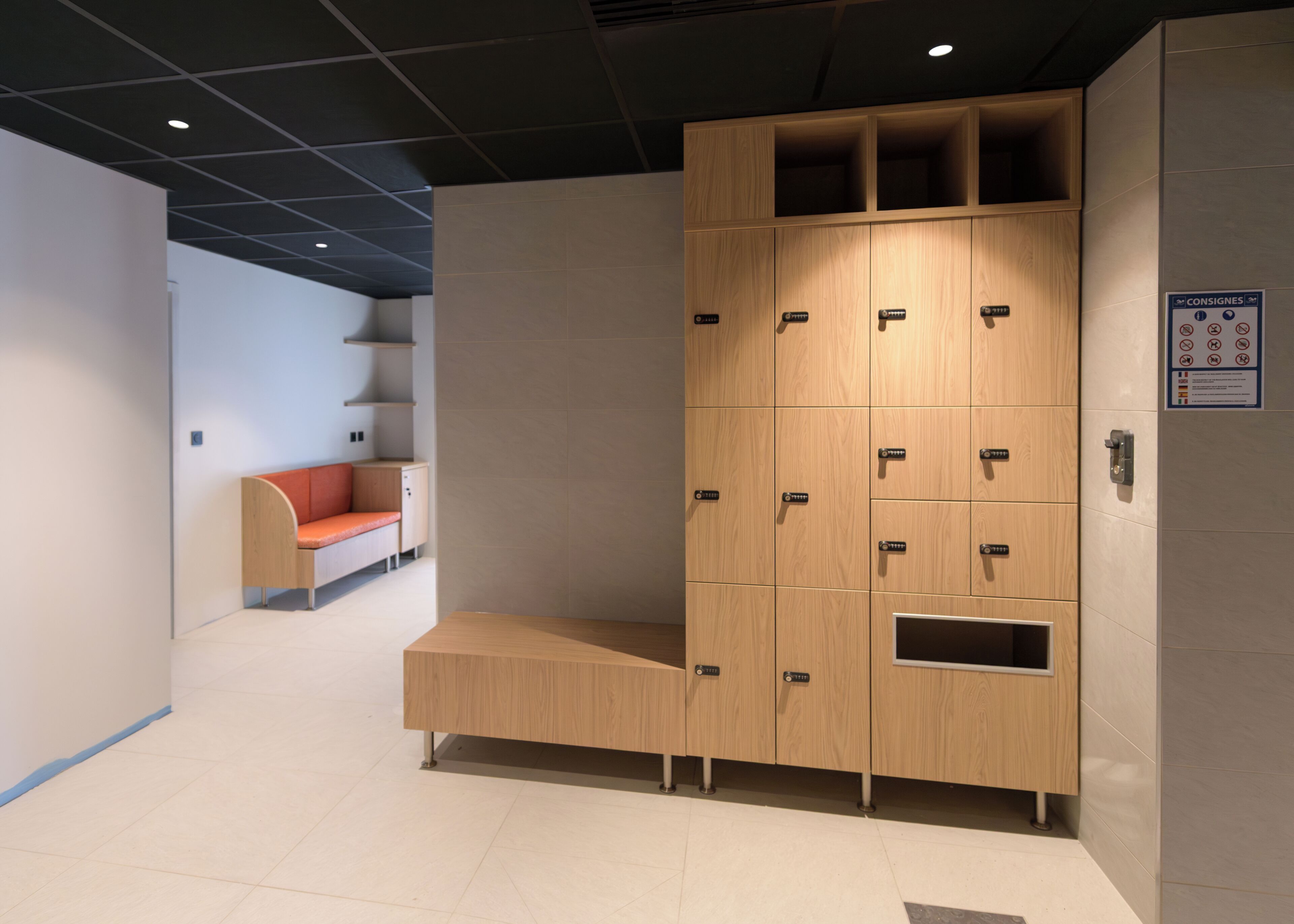 Un vestuario moderno con taquillas de madera, un banco y una zona de estar con un cojín rojo.