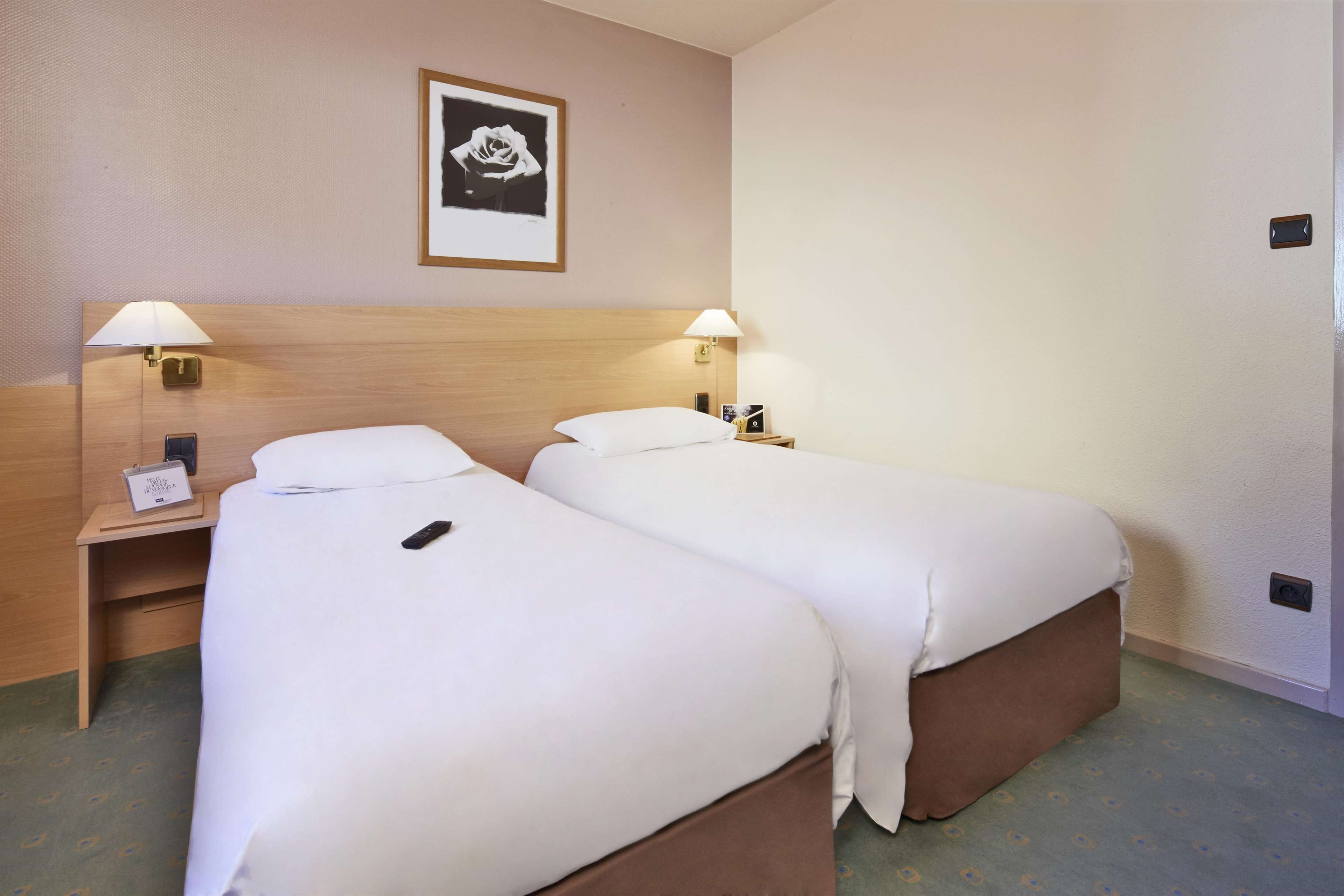 A hotel room with two single beds, bedside tables with lamps, a framed picture on the wall, and a small desk with a phone.