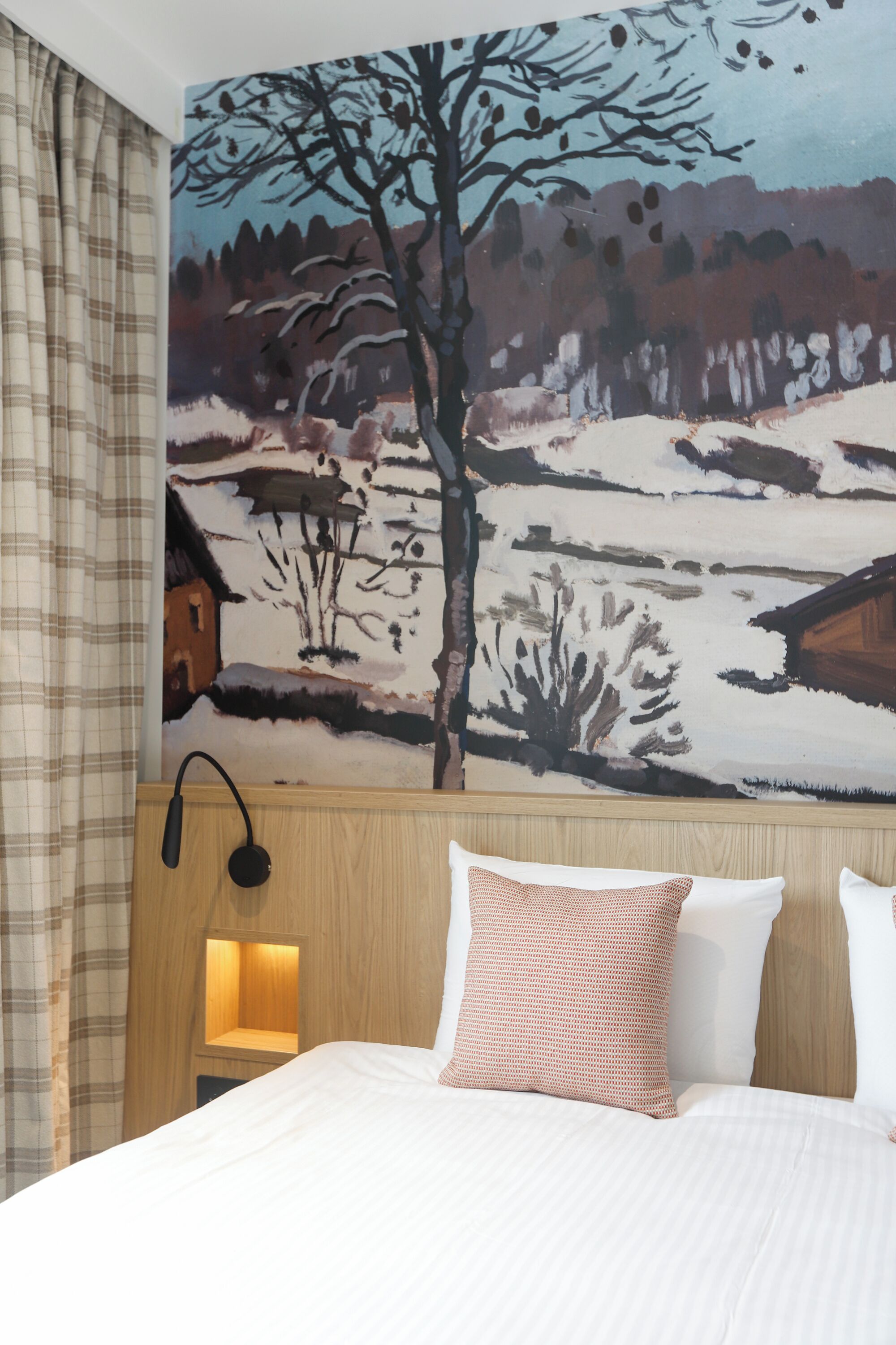 Una habitación de hotel con una cama, un cabecero con una lámpara y un mural en la pared de un paisaje nevado.