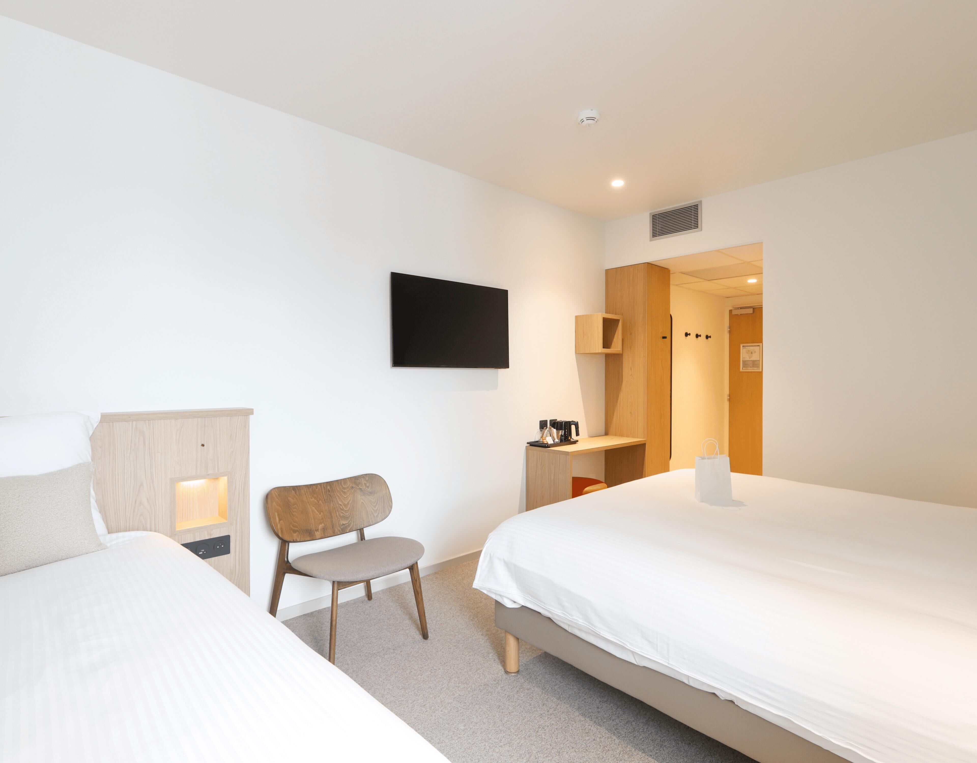 A hotel room with two beds, a chair, a desk, a flat-screen TV, and a door leading to a bathroom.