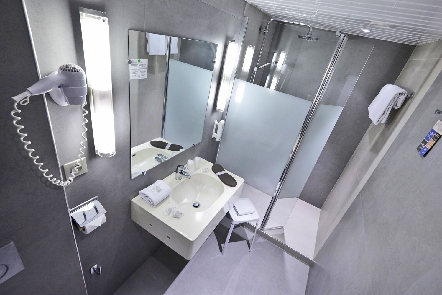 Un baño moderno con un espejo grande, un secador de pelo, un lavamanos y una ducha.