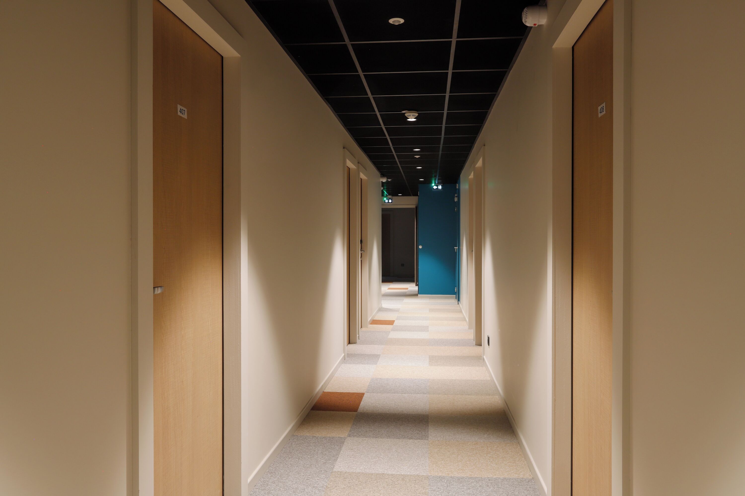 A corridor with doors on both sides, a checkered floor, and a blue wall at the end.