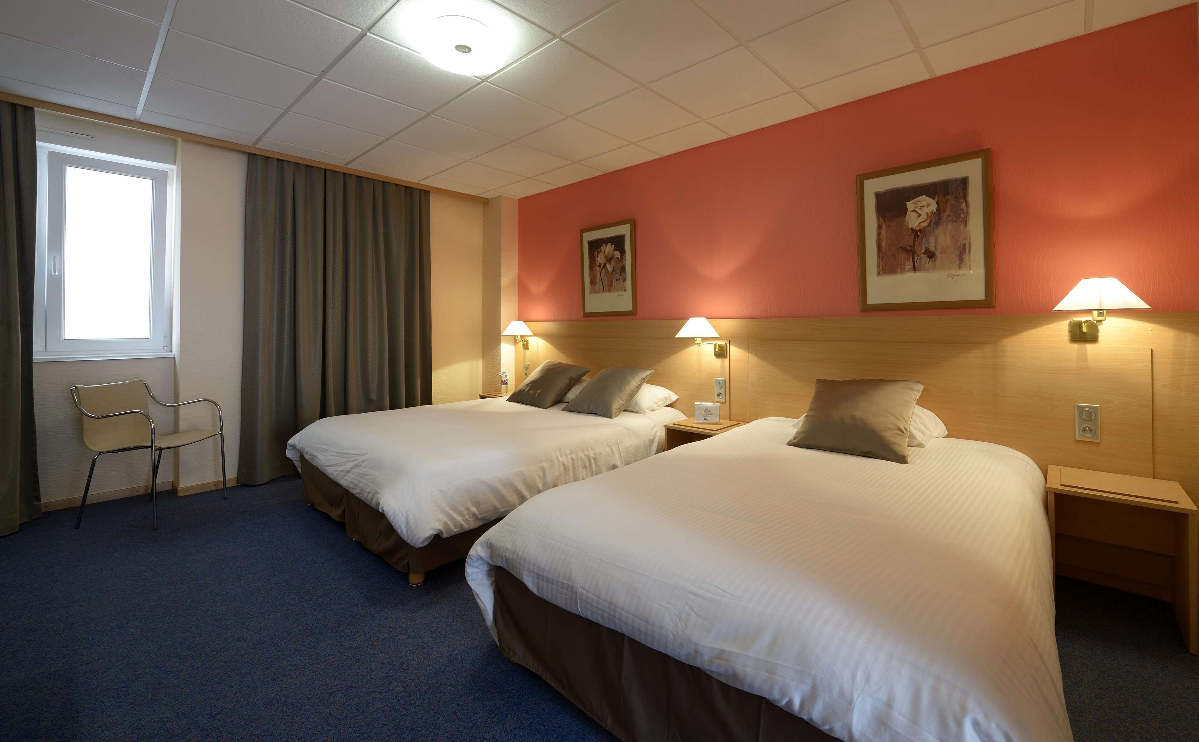 Une chambre d’hôtel avec deux lits, une chaise et une fenêtre avec des rideaux.