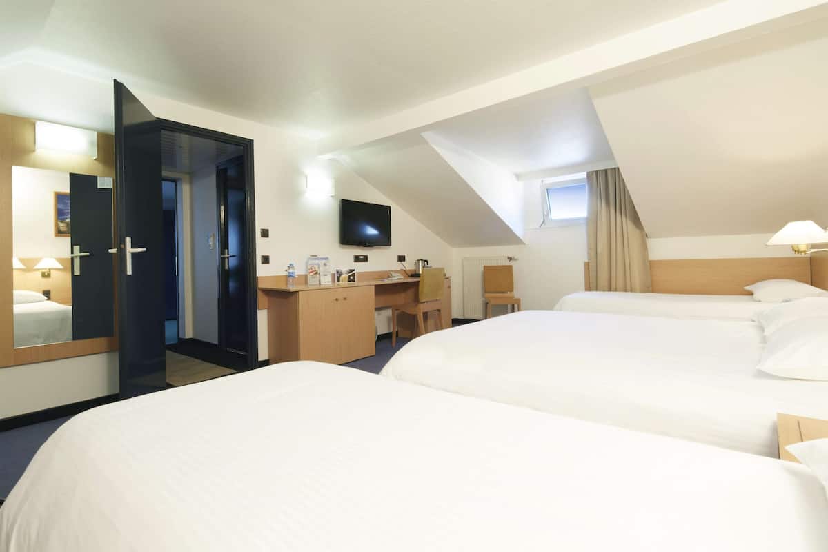 Quarto de hotel com duas camas, uma escrivaninha, uma cadeira, uma televisão e um espelho.