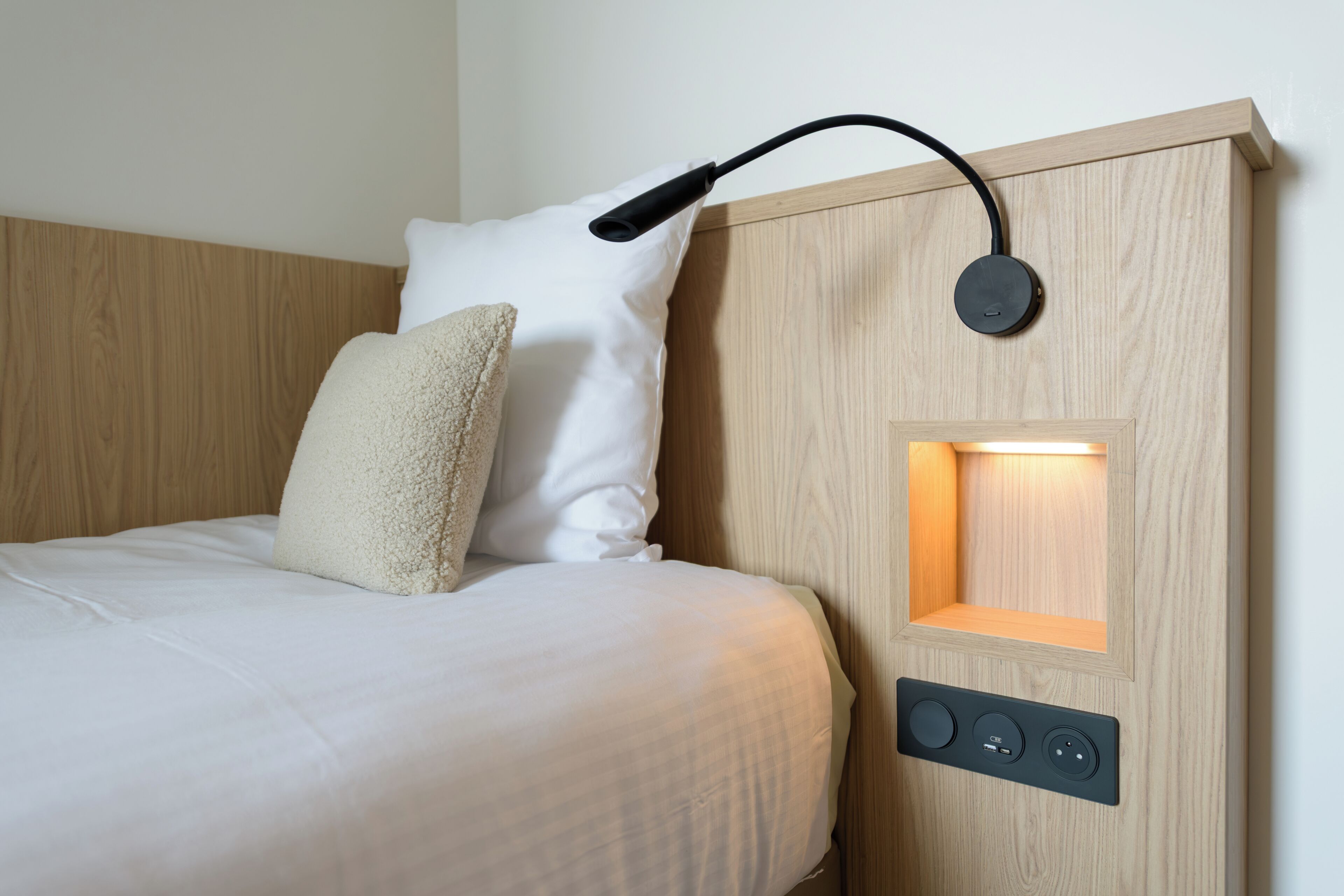Una cama con cabecera que incorpora luz integrada y panel de control.