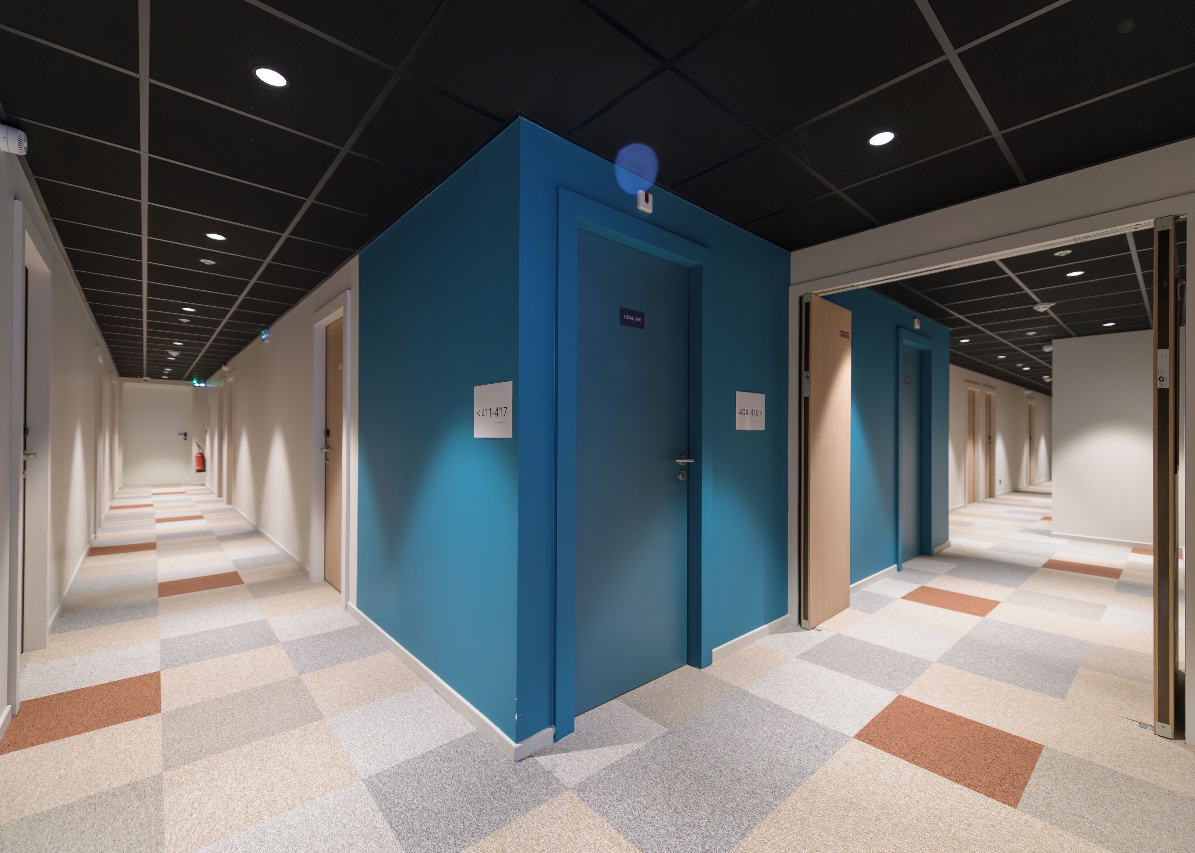 Un pasillo con puertas azules, piso a cuadros e iluminación empotrada en el techo.