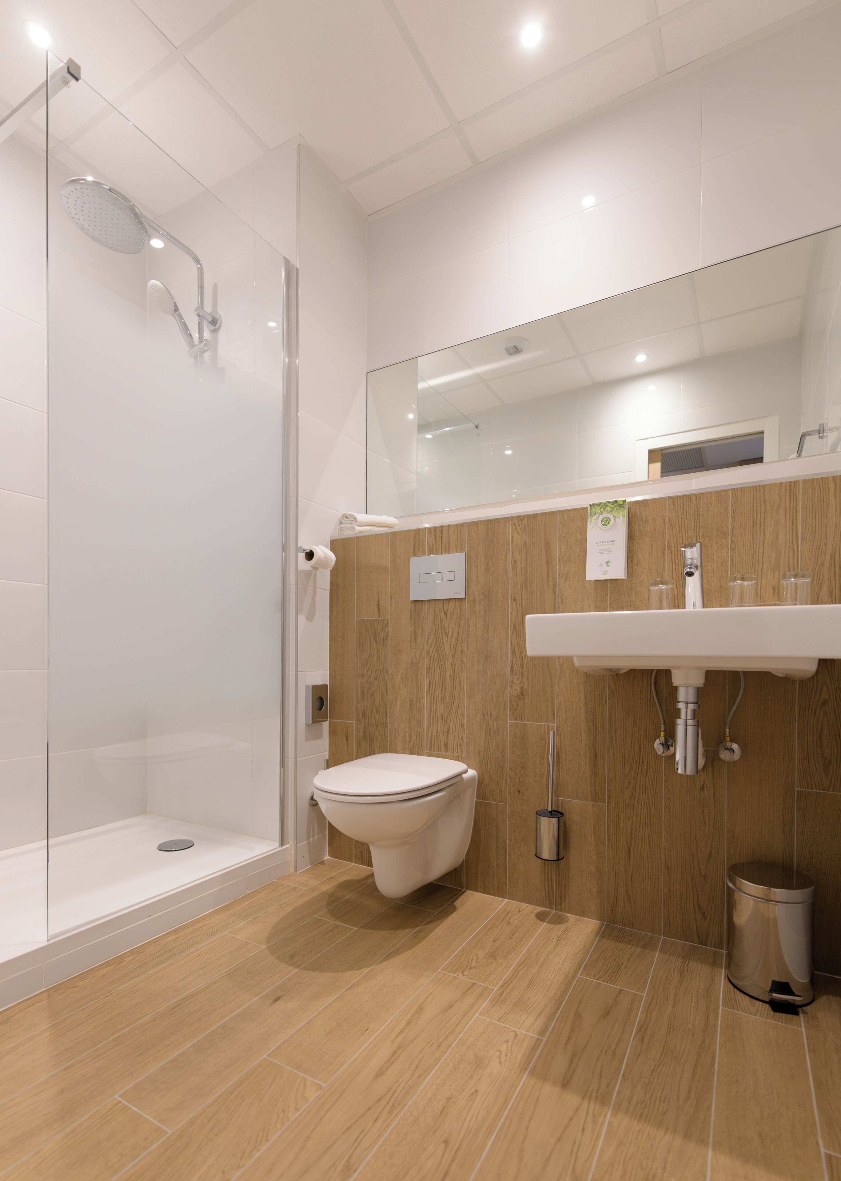 A modern bathroom with a glass shower enclosure, a toilet, and a sink with a wooden panel backdrop.