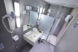 A modern bathroom with a large mirror, a hairdryer, a sink, a shower, and a towel rack. - Kyriad Montbeliard Sochaux (Montbeliard)
