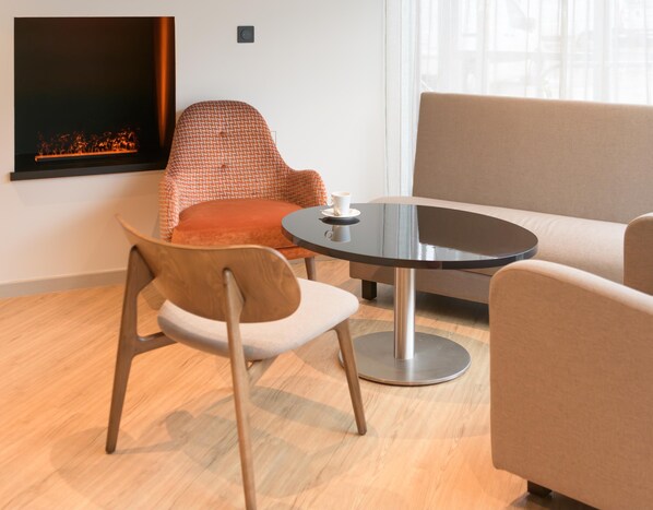 A modern living room with a round table, two chairs, a sofa, and a fireplace. - Kyriad Montbéliard Sochaux Hôtel & Spa (Montbeliard)