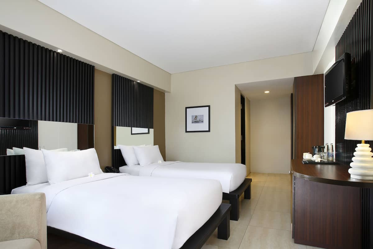 A hotel room with two beds, a desk, a TV, and a framed picture on the wall.