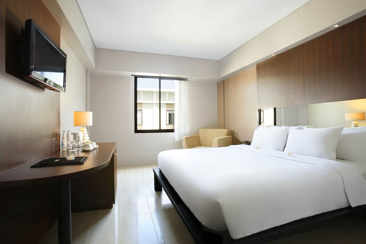 A hotel room with a bed, a desk, a TV, a window, and a view of the building outside.