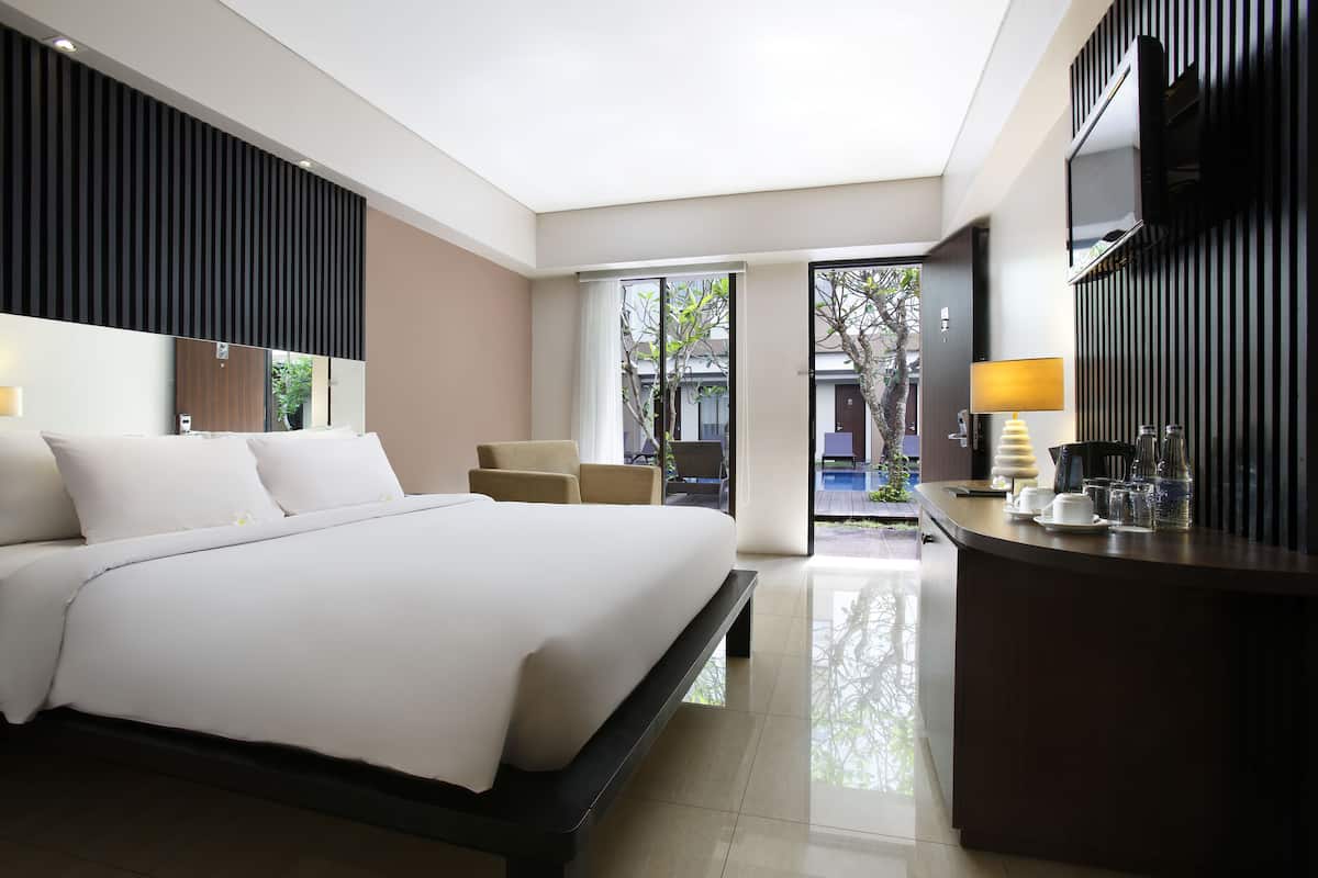 A modern hotel room with a large bed, a desk with a lamp, and a view of the outside.