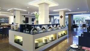 A modern hotel lobby with a buffet area, seating arrangements, and a large window providing natural light. - Hotel Santika Kuta Bali (Kuta)