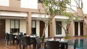 An outdoor dining area with tables and chairs, a pool, and a building with doors and windows. - Hotel Santika Kuta Bali (Kuta)