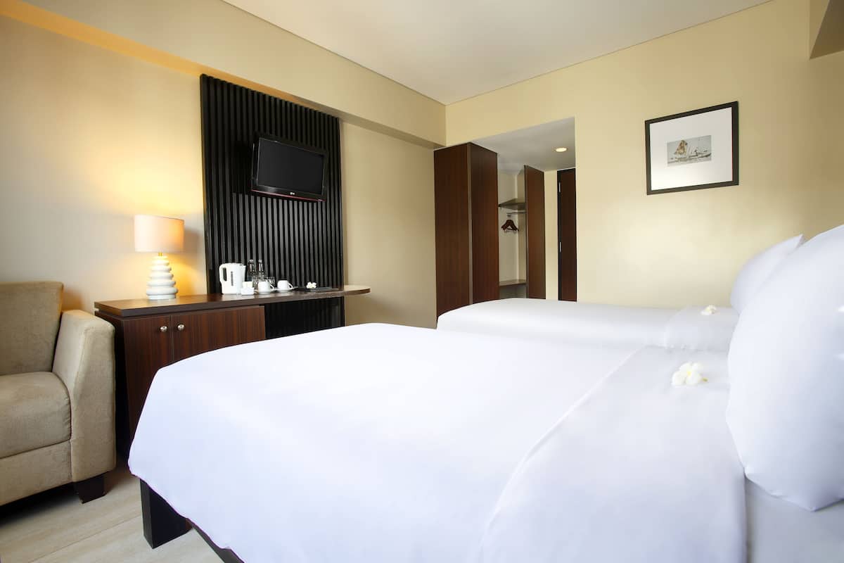 A hotel room with a bed, a desk, a chair, a TV mounted on the wall, and a framed picture.