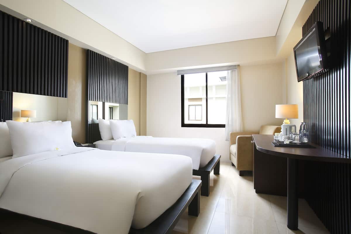 A hotel room with two beds, a desk, a TV, and a window.