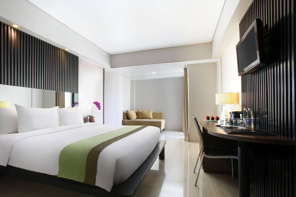 A hotel room with a bed, a desk, a chair, a TV, and a bathroom.