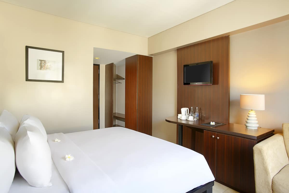 A hotel room with a large bed, a desk with a TV, and a chair.