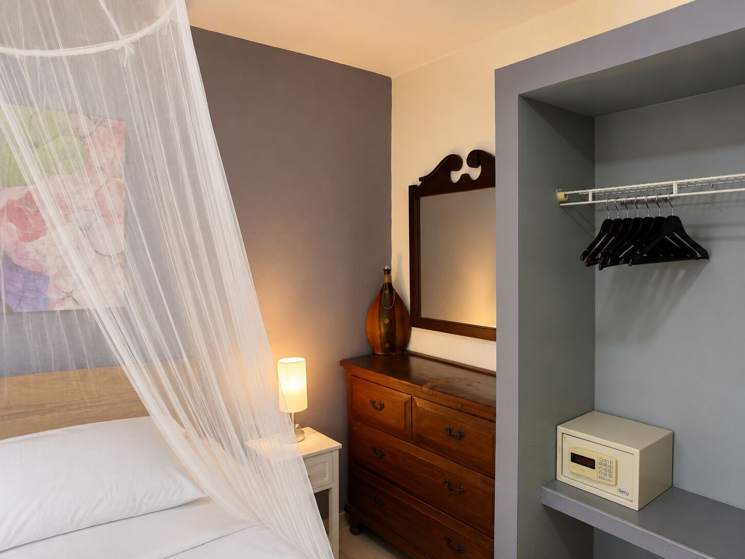 Une chambre d’hôtel comprenant un lit, une table de chevet, une commode, un miroir, une armoire et un thermostat.