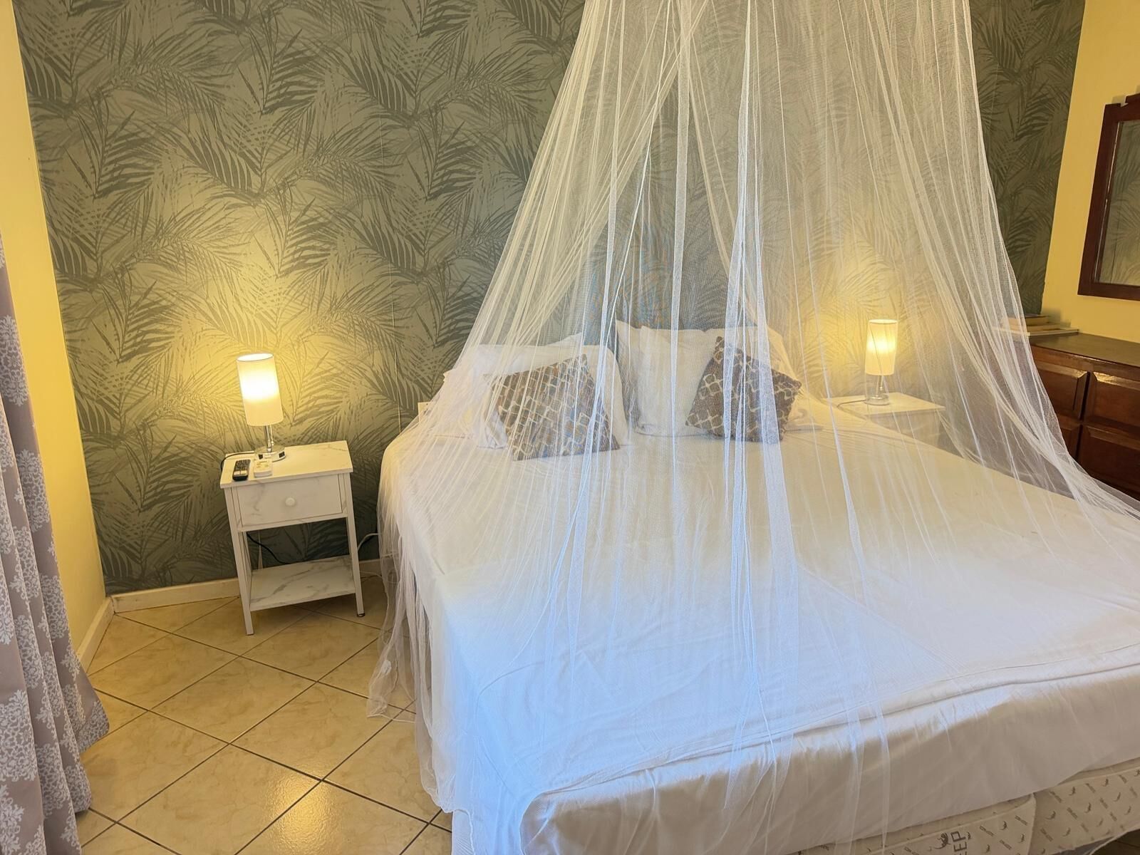 A bed with a canopy, two bedside lamps, a nightstand, and a patterned wall.