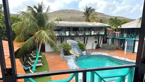 A pool with a slide, a mountain in the background, and a building with a green roof. - Rancho El Sobrino (Sabana Westpunt)