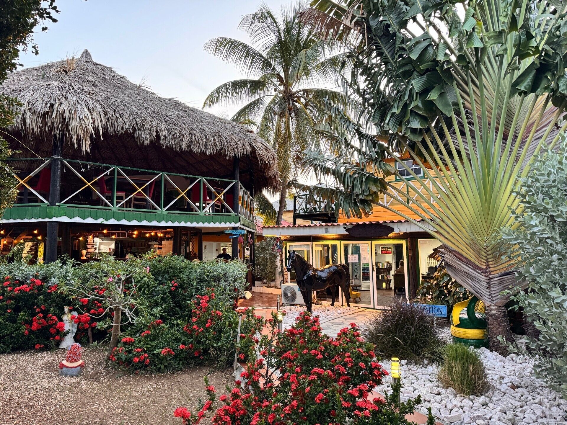 A resort with a thatched-roof building, a horse statue, and a well-maintained garden with red flowers.