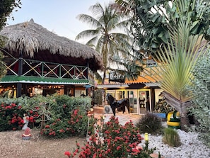 A resort with a thatched-roof building, a horse statue, and a well-maintained garden with red flowers. - Rancho El Sobrino (Sabana Westpunt)