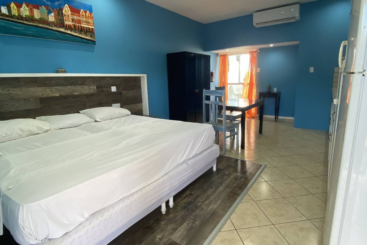 A hotel room with a large bed, a desk with a chair, and a refrigerator.