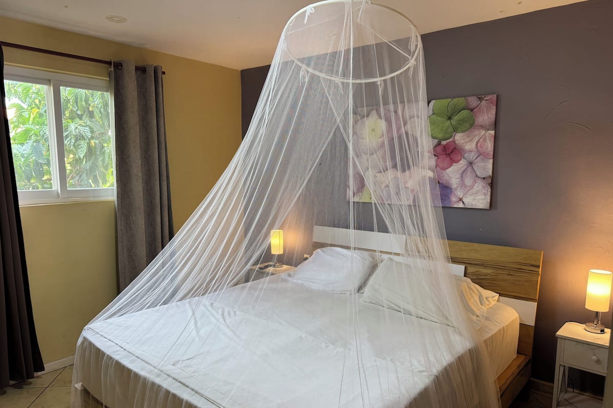 Una cama con dosel, dos lámparas de noche, una mesita de noche y un cuadro con motivos florales en la pared.