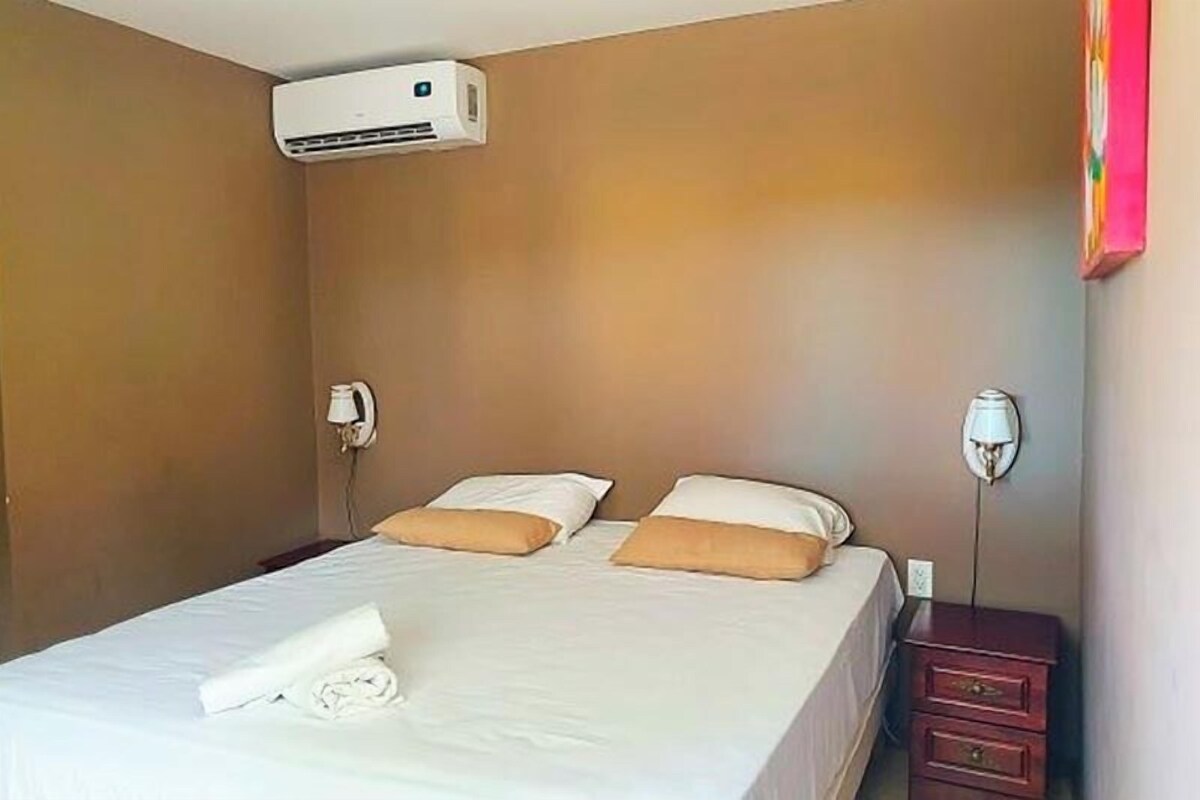 A hotel room with a bed, a bedside lamp, a telephone, and an air conditioning unit.