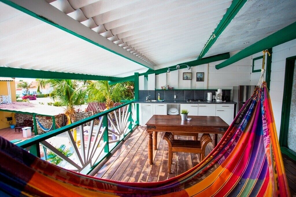 A covered outdoor area with a wooden table, a hammock, and a kitchen area with white cabinets.