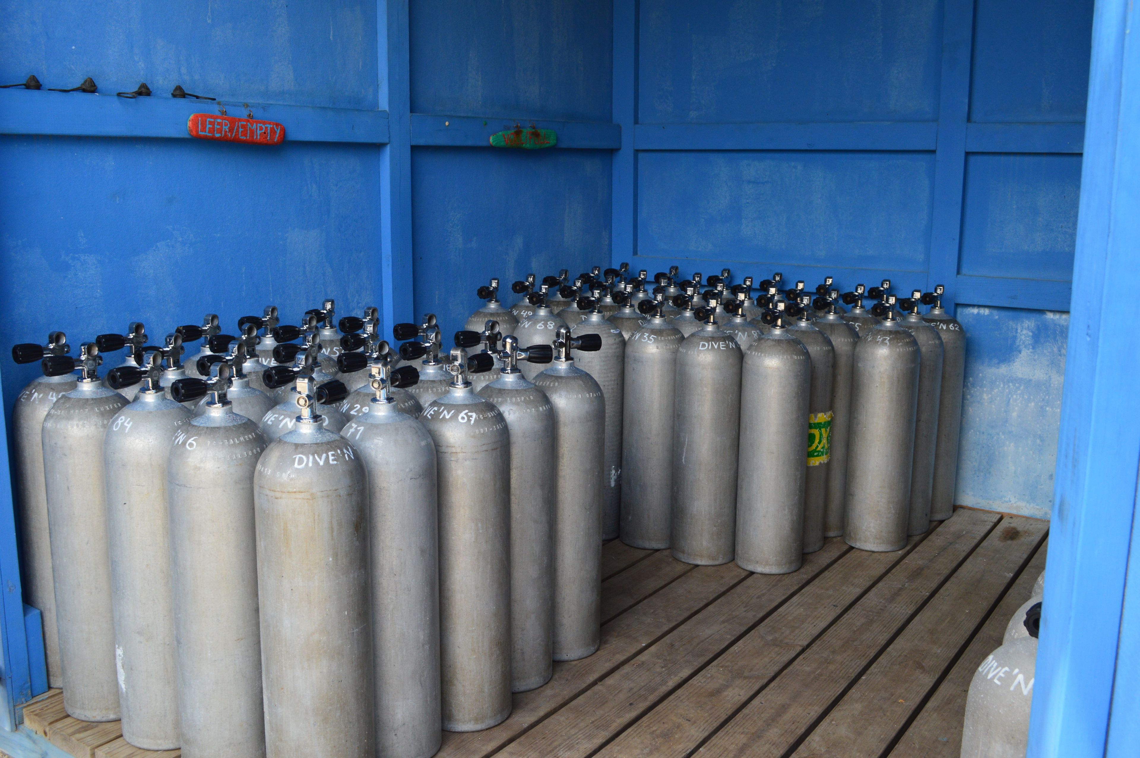 A row of metal oxygen tanks labeled 'DIVE'N' in a blue container with a wooden floor.