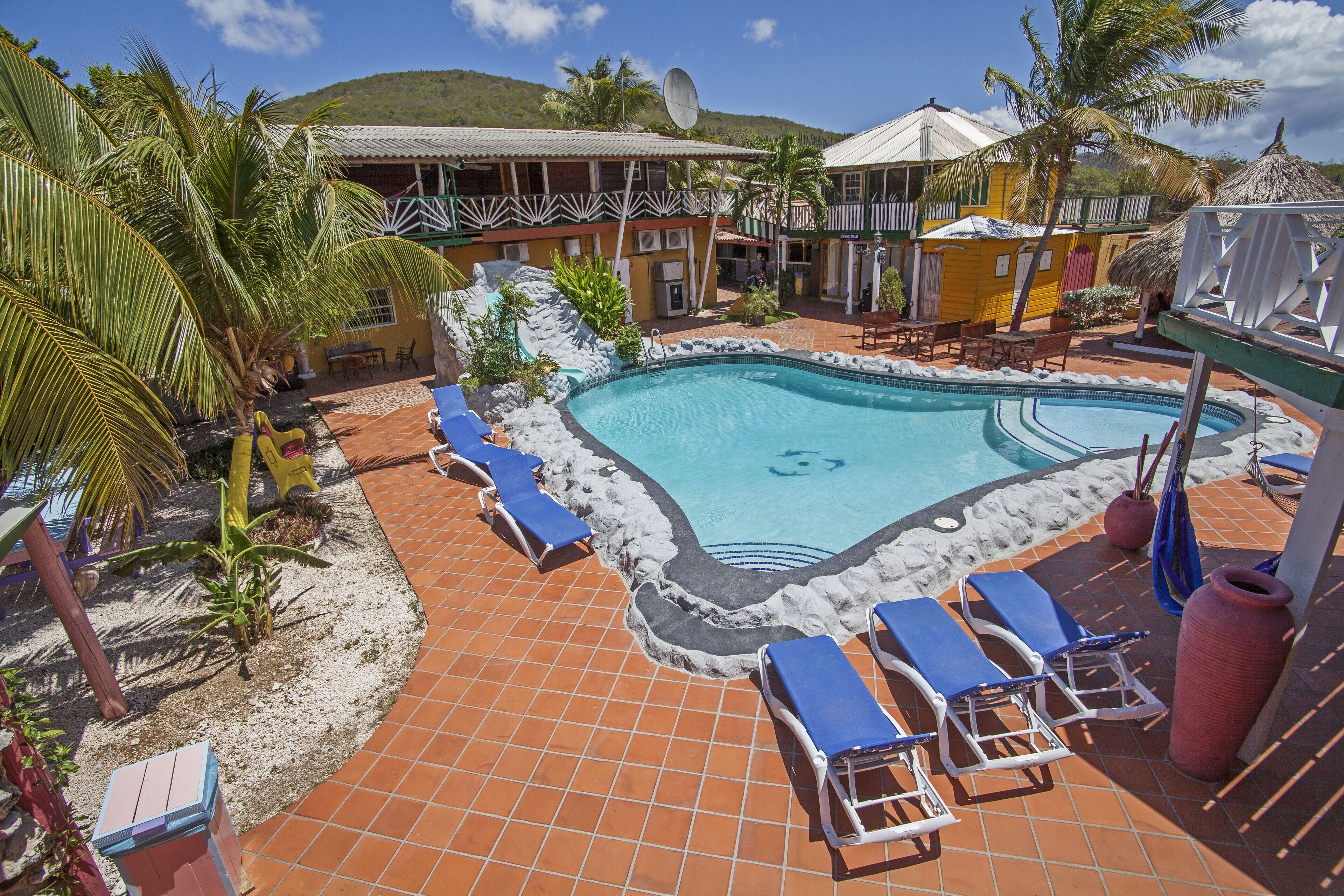 A pool area with lounge chairs, a small pool, and a building with a thatched roof.